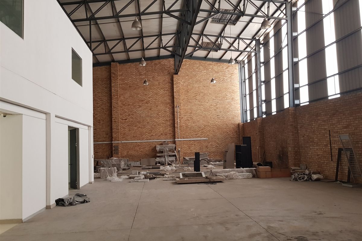 Spacious industrial warehouse unit featuring high ceilings with exposed steel trusses, brick walls, concrete flooring, and large windows providing ample natural light.