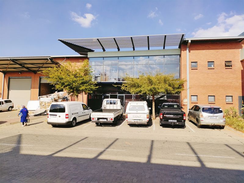 Front elevation of an industrial property featuring a brick facade, large glass curtain wall, louvred canopy, and a paved parking area.