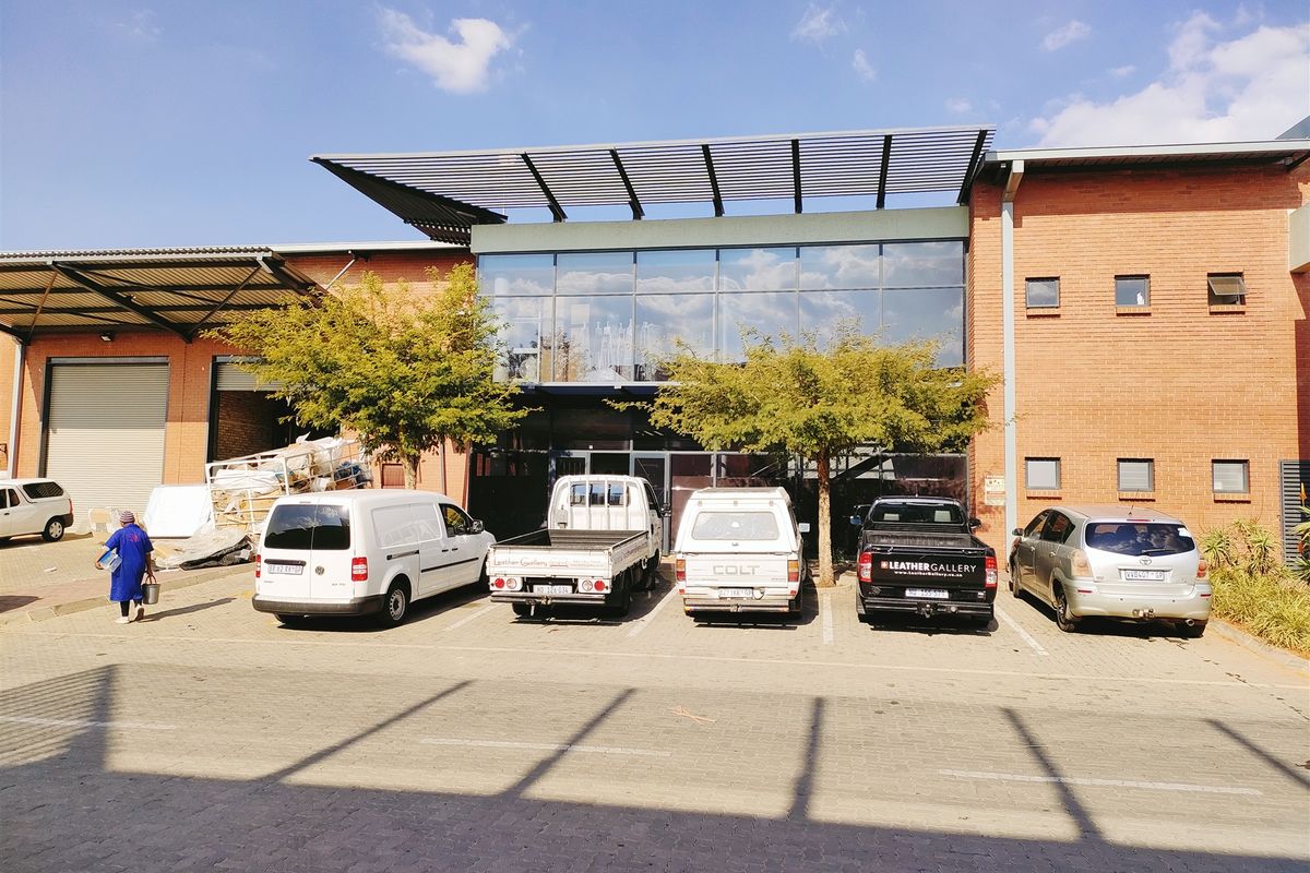 Front elevation of an industrial property featuring a brick facade, large glass curtain wall, louvred canopy, and a paved parking area.