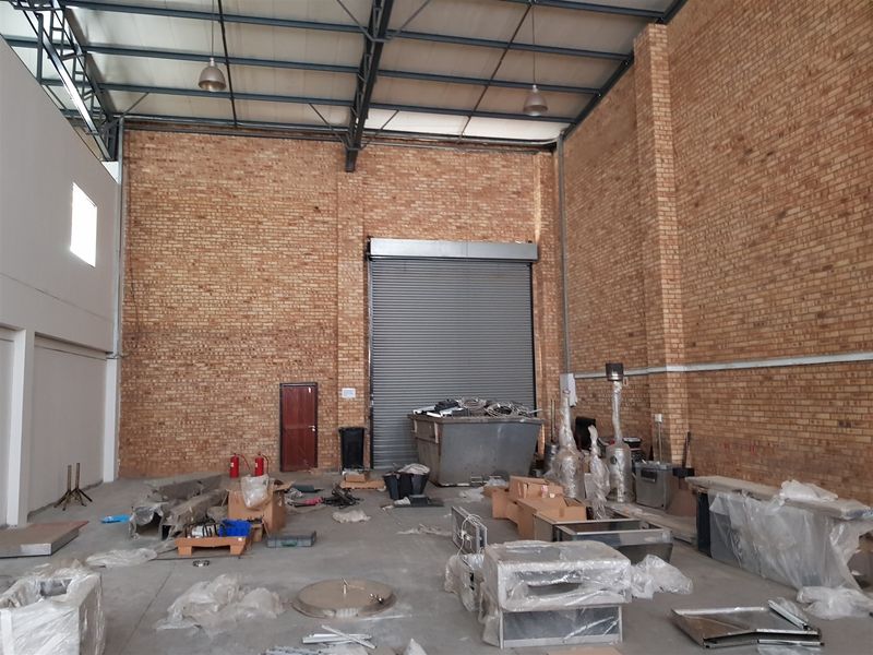 Spacious industrial warehouse unit featuring high ceilings, exposed brickwork, concrete flooring, and a large roller shutter door for easy access.