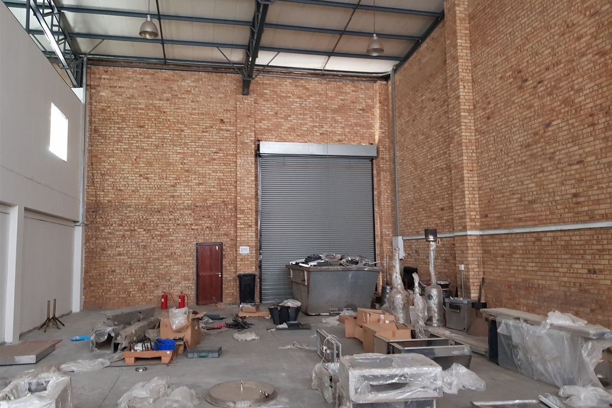 Spacious industrial warehouse unit featuring high ceilings, exposed brickwork, concrete flooring, and a large roller shutter door for easy access.