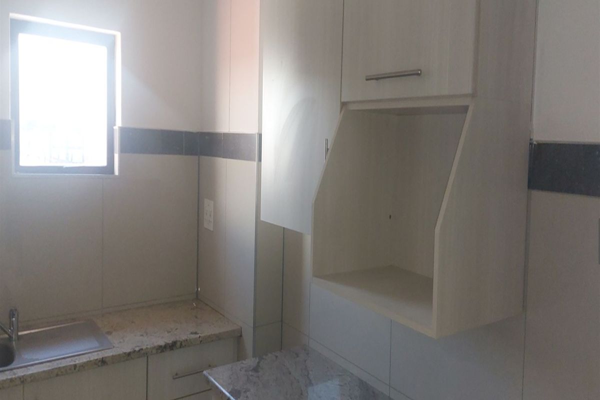 A clean, functional kitchen area featuring light-toned built-in cabinetry, granite countertops, and a stainless steel sink with tiled backsplash.
