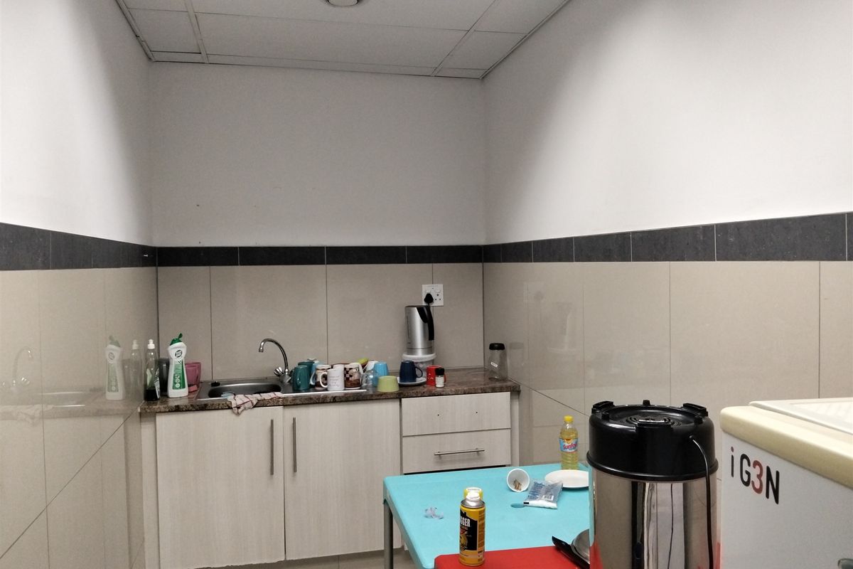A functional kitchenette area featuring built-in cabinetry, a stainless steel sink, and tiled splashback finishes within an industrial office setting.