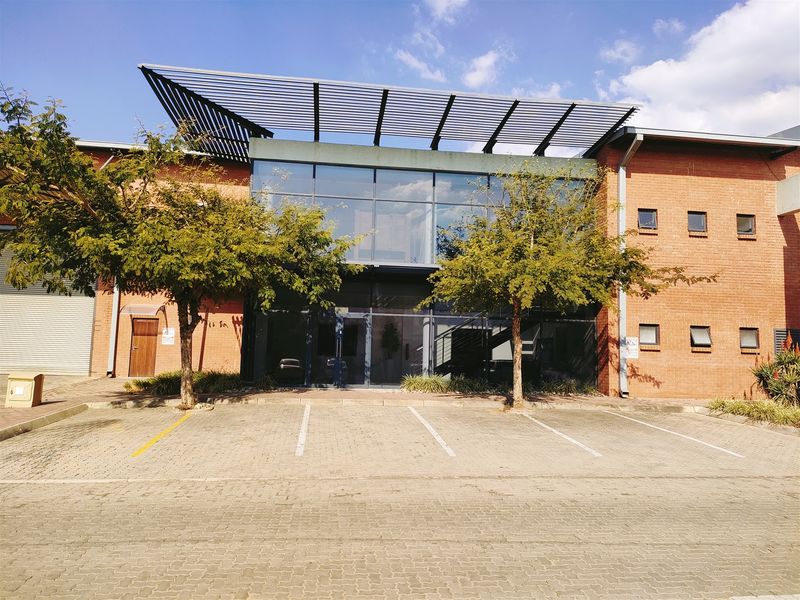 Front elevation of an industrial property featuring a modern glass facade, brick construction, metal canopy, and dedicated paved parking bays.