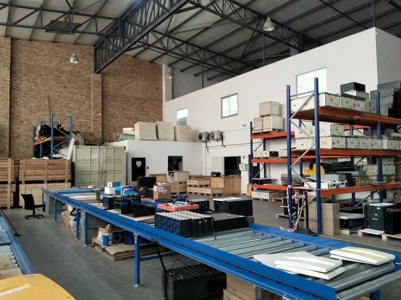 Spacious industrial warehouse featuring exposed steel roof trusses, brick wall detailing, heavy-duty pallet racking, and an integrated roller conveyor system for efficient operations.