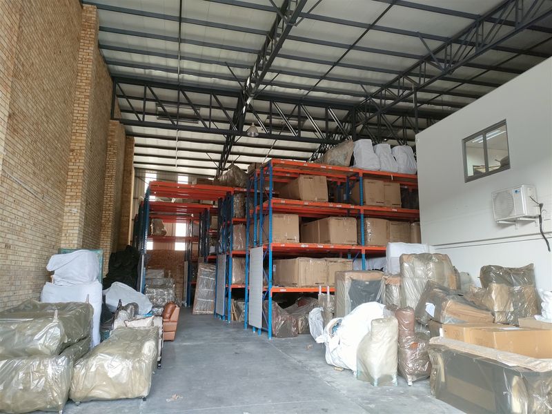 Spacious industrial warehouse featuring high ceilings with exposed steel trusses, concrete flooring, and extensive built-in racking systems for storage.