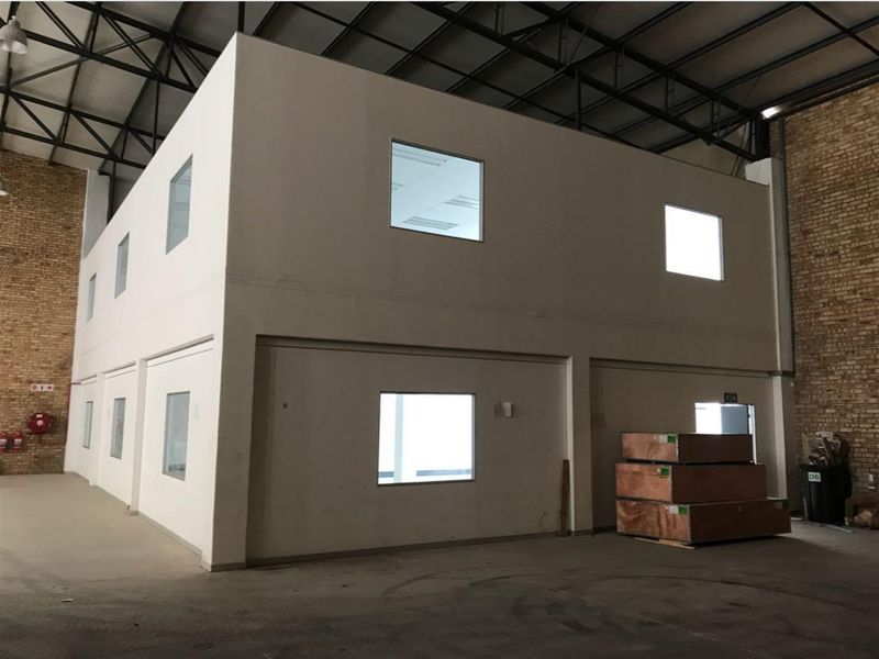 A large industrial warehouse space featuring a two-story internal office structure, exposed steel roof trusses, and durable concrete flooring.