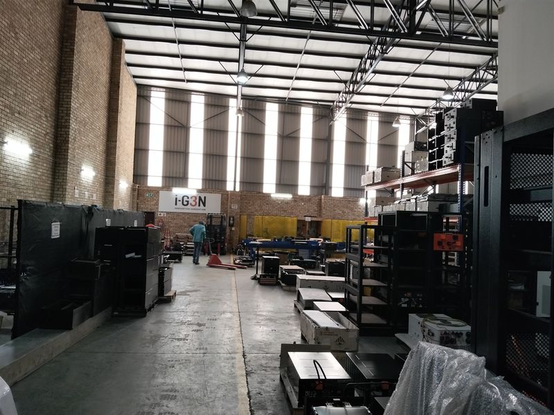 Spacious industrial warehouse facility featuring high ceilings with exposed steel trusses, concrete flooring, and natural light through translucent roof panels.