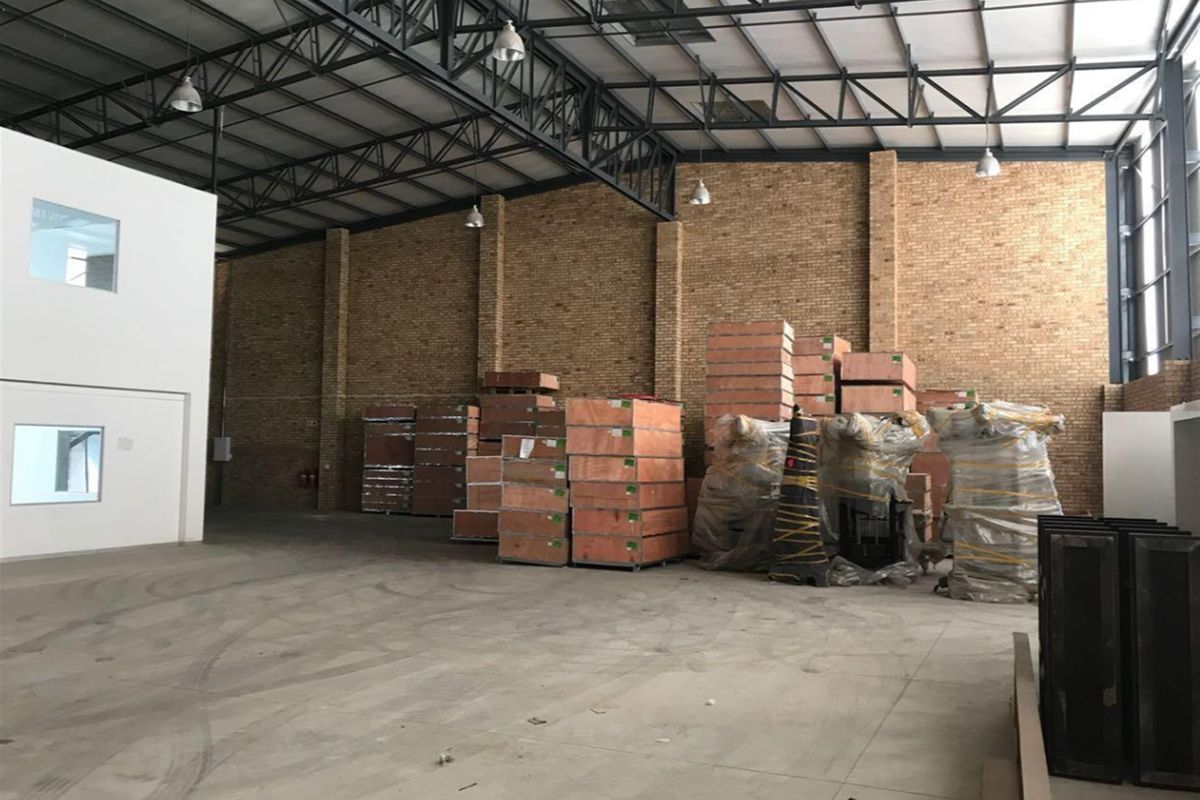 Spacious industrial warehouse featuring high exposed steel roof trusses, brick wall finishes, and durable concrete flooring, suitable for storage or manufacturing operations.