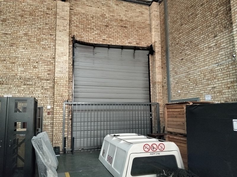 Industrial utility space featuring high exposed brick walls and a large roller shutter door with integrated security gate.