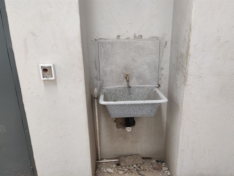 A basic utility area featuring a wall-mounted sink with exposed plumbing and unfinished wall surfaces, suitable for industrial or workshop use.