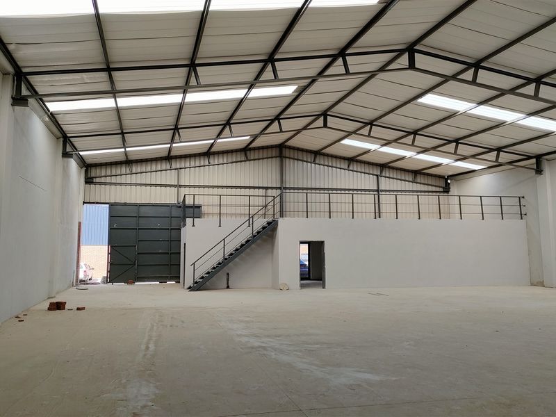 Spacious industrial warehouse featuring a high-clearance steel truss roof with integrated skylights, a mezzanine level with staircase, and a large roller door access.