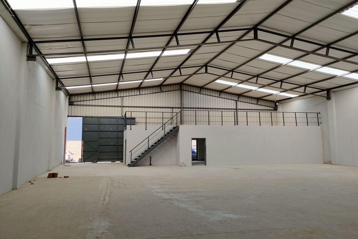 Spacious industrial warehouse featuring a high-clearance steel truss roof with integrated skylights, a mezzanine level with staircase, and a large roller door access.