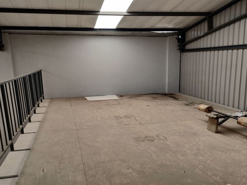 An industrial mezzanine level featuring a metal structure, corrugated wall cladding, and a skylight, providing an open utility space.