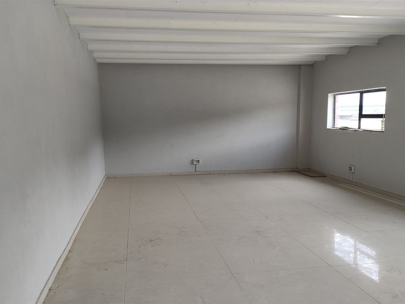 An empty, open-plan industrial space featuring tiled flooring, exposed ceiling beams, and natural light from side windows.
