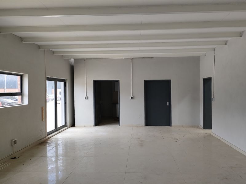 A spacious, empty open-plan industrial unit featuring tiled flooring, exposed beam ceilings, and multiple access points through aluminium-framed doors.