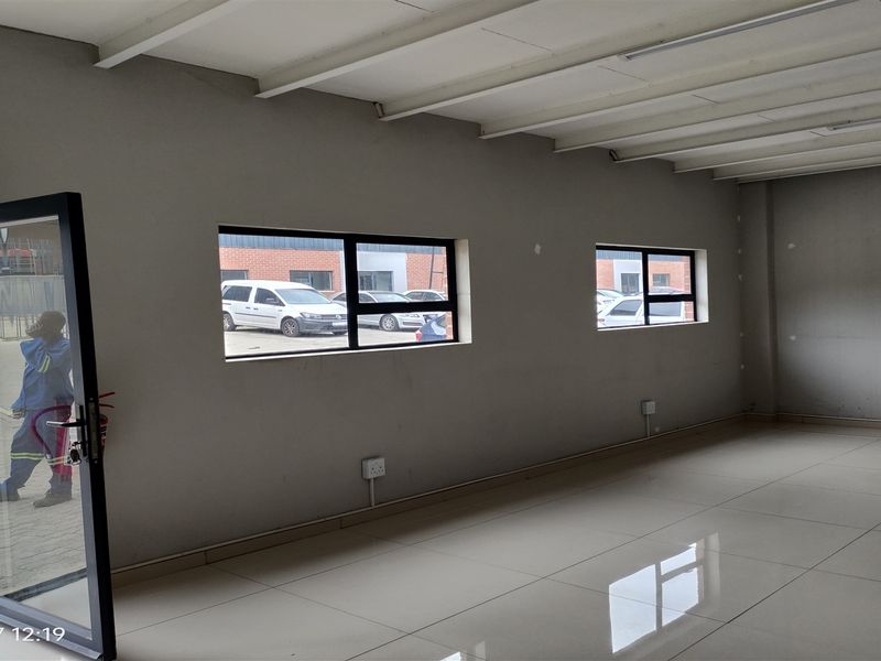 An open-plan industrial utility space featuring tiled flooring, exposed beam ceilings, and large windows providing natural light.
