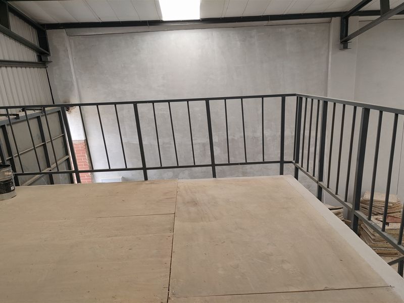 An industrial mezzanine level featuring a metal safety railing, exposed steel roof structure, and a skylight, currently in an unfinished state.
