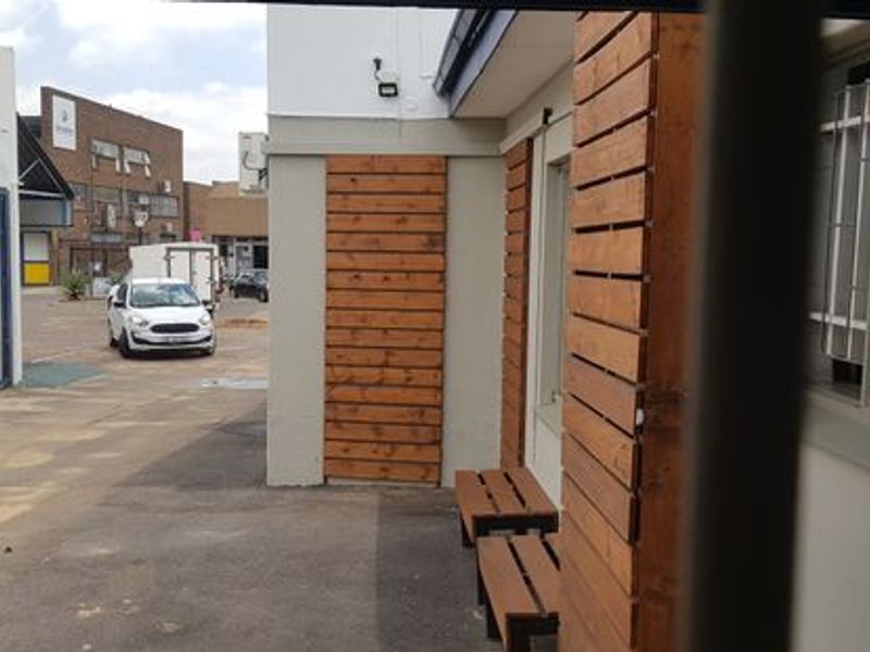Rear exterior view of the office building featuring timber cladding accents, paved courtyard area, and security bars on windows.
