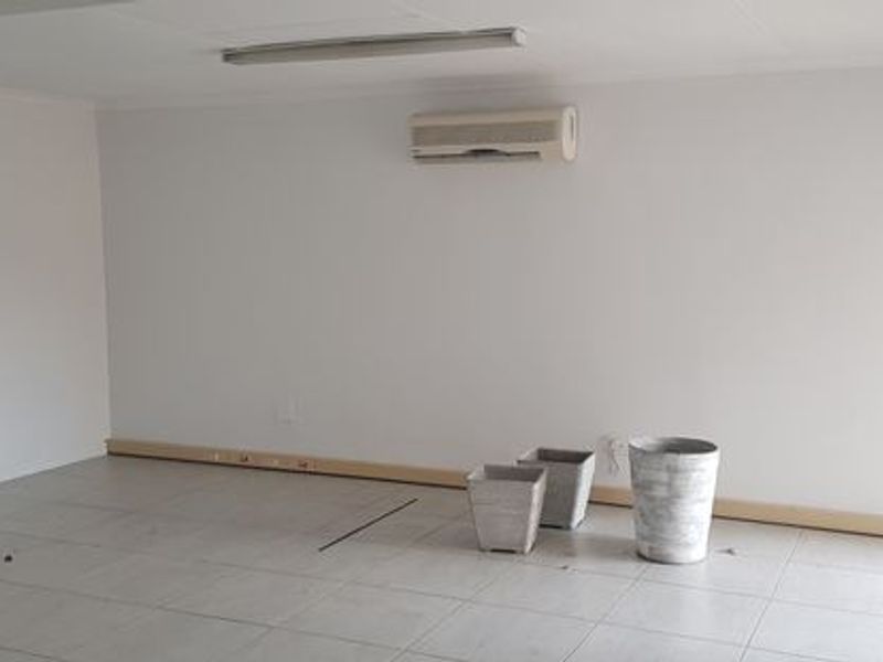 A clean, empty office space featuring tiled flooring, a wall-mounted air conditioning unit, and a fire extinguisher.