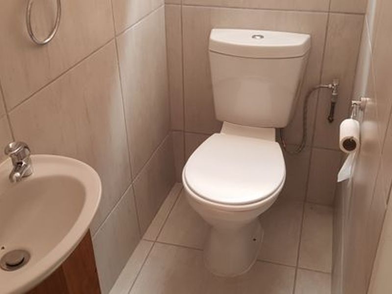A compact, well-maintained guest bathroom featuring neutral wall and floor tiles, a modern ceramic toilet, and a wall-mounted basin.