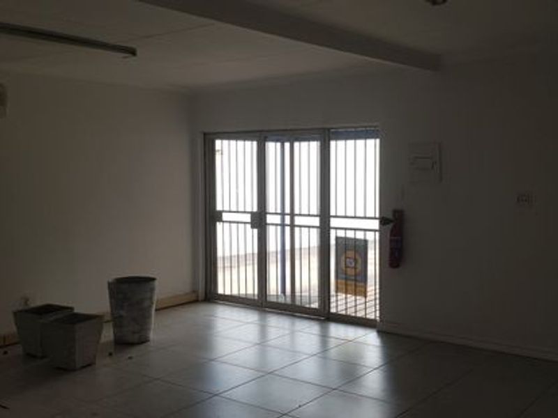 An empty office space featuring tiled flooring, an air conditioning unit, and a secure sliding glass door entrance.
