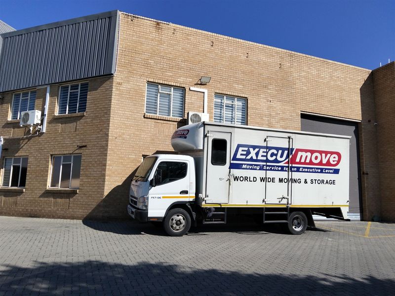 Front elevation of an industrial property featuring face brick construction, steel-framed windows, a roller shutter door, and external air conditioning units.