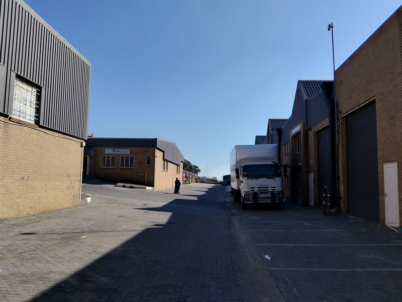 Exterior view of an industrial complex featuring brick buildings, paved access roads, and metal roller shutter doors for loading and logistics.