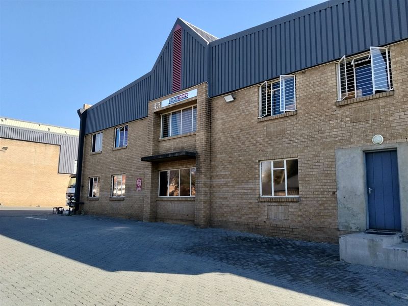 Front elevation of a two-story industrial building featuring face brick construction, metal roof cladding, and a paved driveway area.