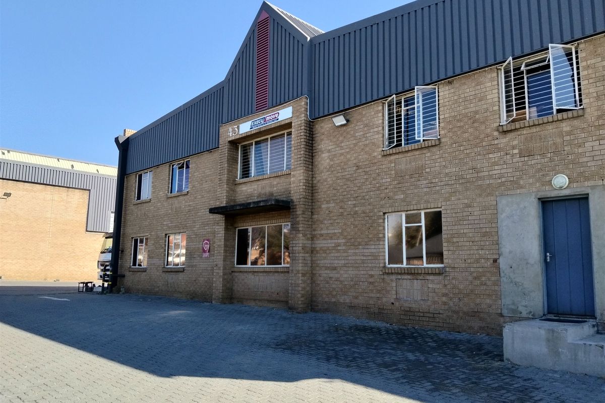 Front elevation of a two-story industrial building featuring face brick construction, metal roof cladding, and a paved driveway area.
