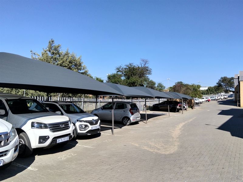 Outdoor parking area featuring multiple shade cloth carports, paved surfacing, and secure steel palisade perimeter fencing.