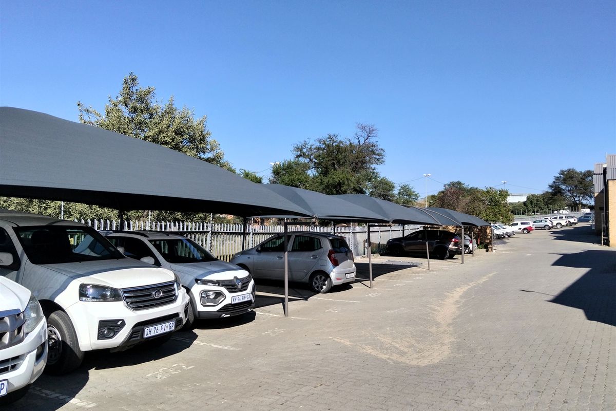 Outdoor parking area featuring multiple shade cloth carports, paved surfacing, and secure steel palisade perimeter fencing.