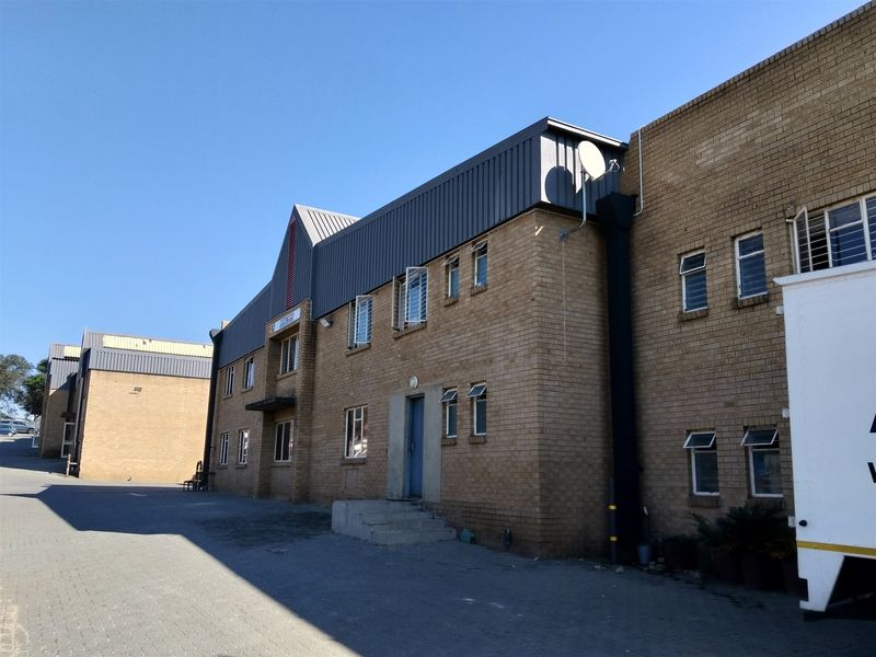 Exterior view of a multi-story industrial building featuring face brick construction, metal roof cladding, and paved driveway access.