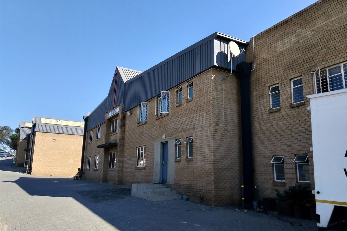 Exterior view of a multi-story industrial building featuring face brick construction, metal roof cladding, and paved driveway access.