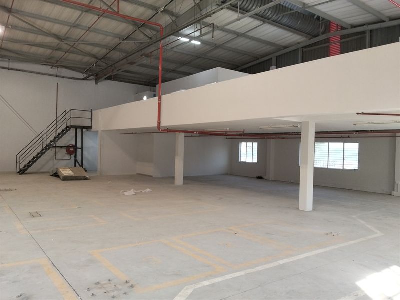 Spacious industrial utility area featuring a mezzanine level, concrete flooring, exposed fire sprinkler piping, and a metal staircase for access.