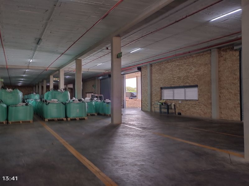 Spacious industrial warehouse featuring concrete flooring, exposed structural columns, fire sprinkler systems, and large roller shutter access points.