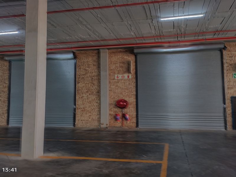 Spacious industrial utility area featuring exposed brick walls, concrete flooring, multiple roller shutter doors, and integrated fire safety equipment.