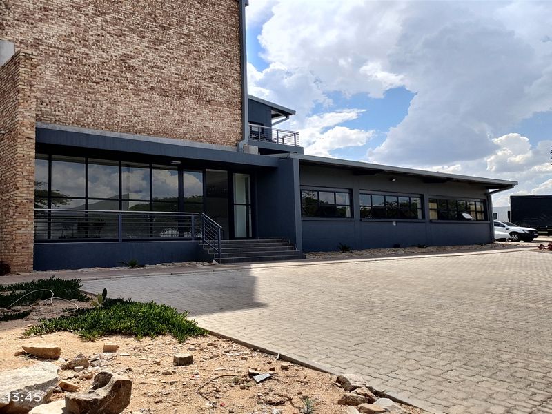 Modern industrial building exterior featuring a combination of exposed brick and dark painted finishes with extensive glazing and a paved parking area.