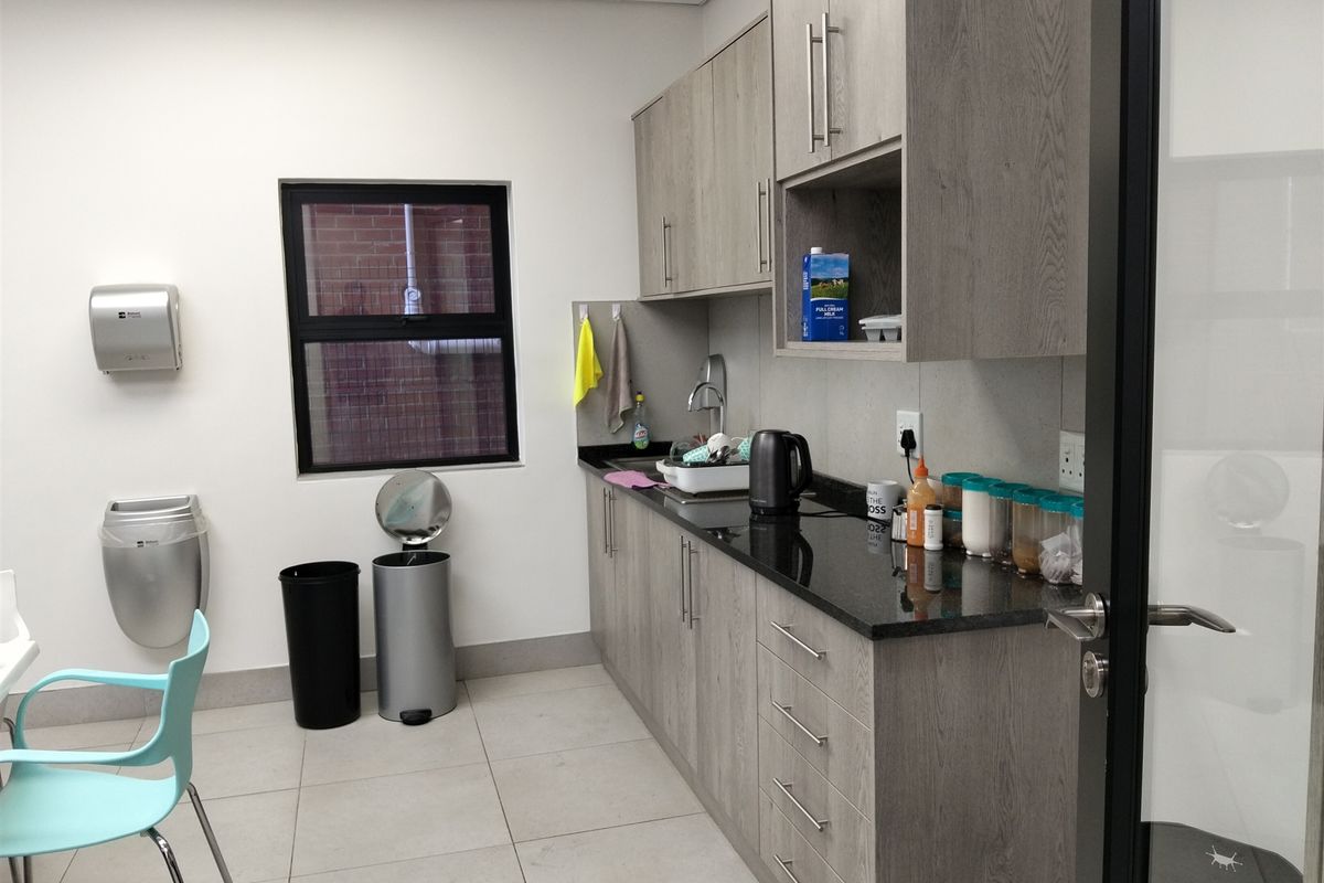 A functional kitchenette featuring modern grey cabinetry, granite countertops, a stainless steel sink, and tiled flooring, suitable for office or industrial utility use.