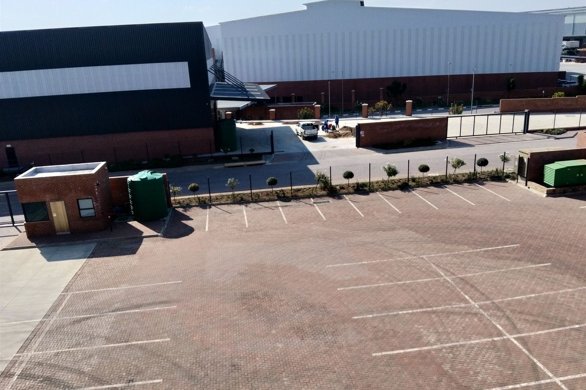 Aerial view of an industrial property featuring a large paved parking area, security guard house, and modern warehouse facility with perimeter fencing.