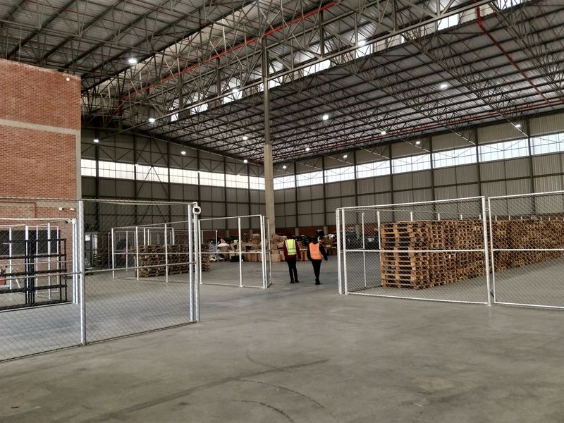 Spacious industrial warehouse featuring high-clearance steel truss roofing, polished concrete floors, and secure internal chain-link partitioned storage areas.
