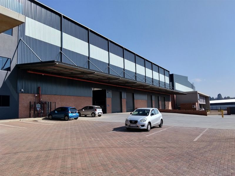 Industrial warehouse facility featuring a brick and metal clad facade, multiple roller shutter doors, and a paved exterior parking area.