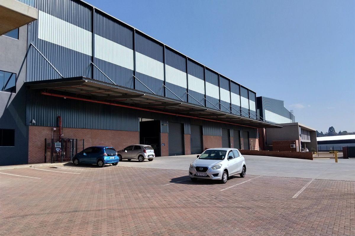 Industrial warehouse facility featuring a brick and metal clad facade, multiple roller shutter doors, and a paved exterior parking area.