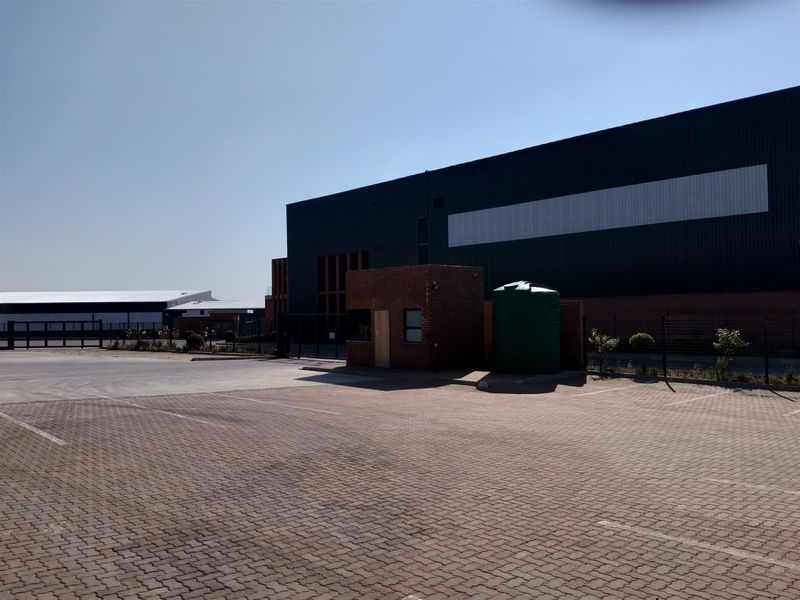 Industrial property exterior featuring a paved parking area, security guard house, and large metal-clad warehouse structure with an integrated water storage tank.