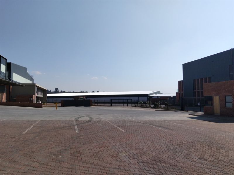 Wide view of an industrial property featuring paved parking area, secure gated access, and large warehouse structures.