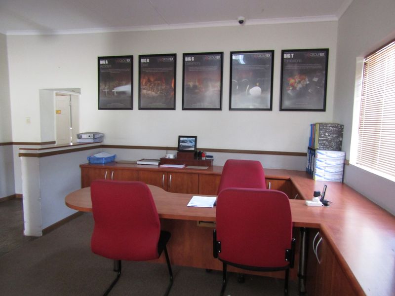 A functional office space featuring a built-in wooden desk, partition wall, and venetian blinds, providing a professional environment for administrative tasks.