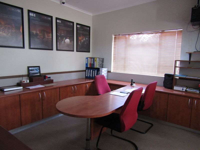 A functional office space featuring extensive built-in wooden cabinetry, neutral wall finishes, and venetian blinds providing natural light.