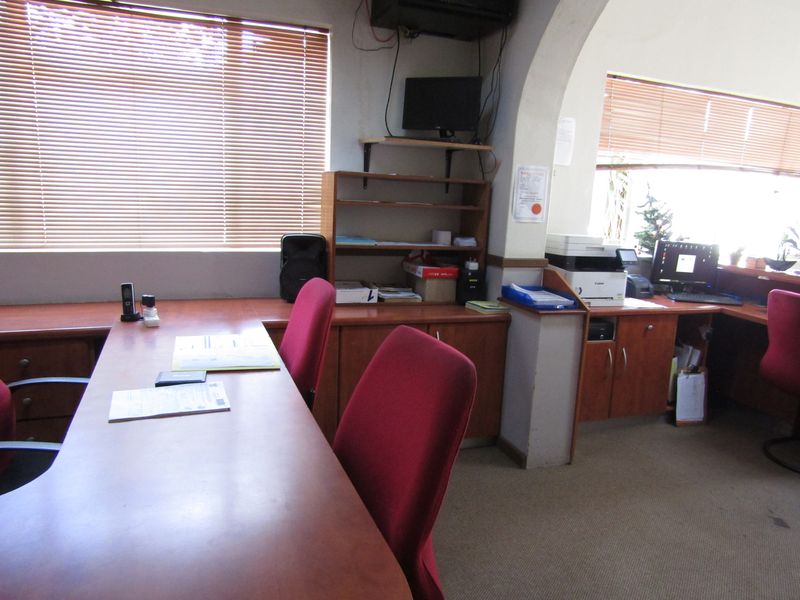A functional office space featuring built-in wooden cabinetry, carpeted flooring, and large windows with venetian blinds, providing a practical workspace environment.