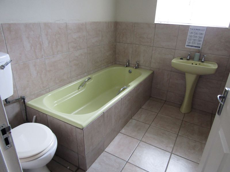 A dated bathroom featuring a pale yellow bathtub and matching pedestal basin, complemented by neutral ceramic wall and floor tiling.