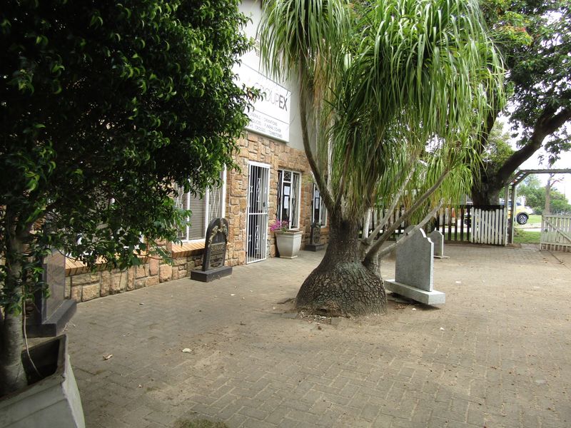 Front exterior view of the office building featuring stone cladding, a paved courtyard area, and secure entrance gates.